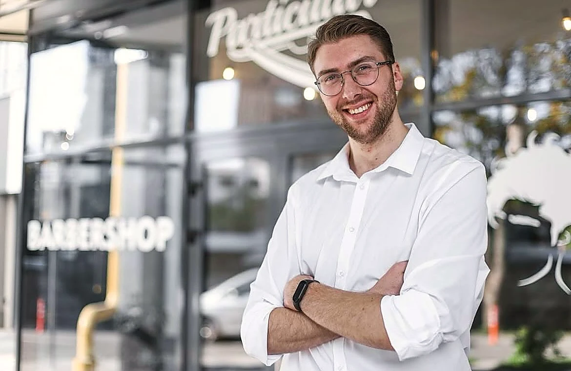 El dueño de Barbería Particular sonriendo delante del escaparate de la barbería